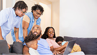 Image of an immediate family gathering with their extended family members looking at a laptop computer
